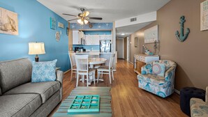 A living room with a sofa, a coffee table, and a patterned armchair. There is a dining area with a table and chairs. - Windy Shores-Oceanfront 2BD Condo-Pool-Pet Friendly (North Myrtle Beach)