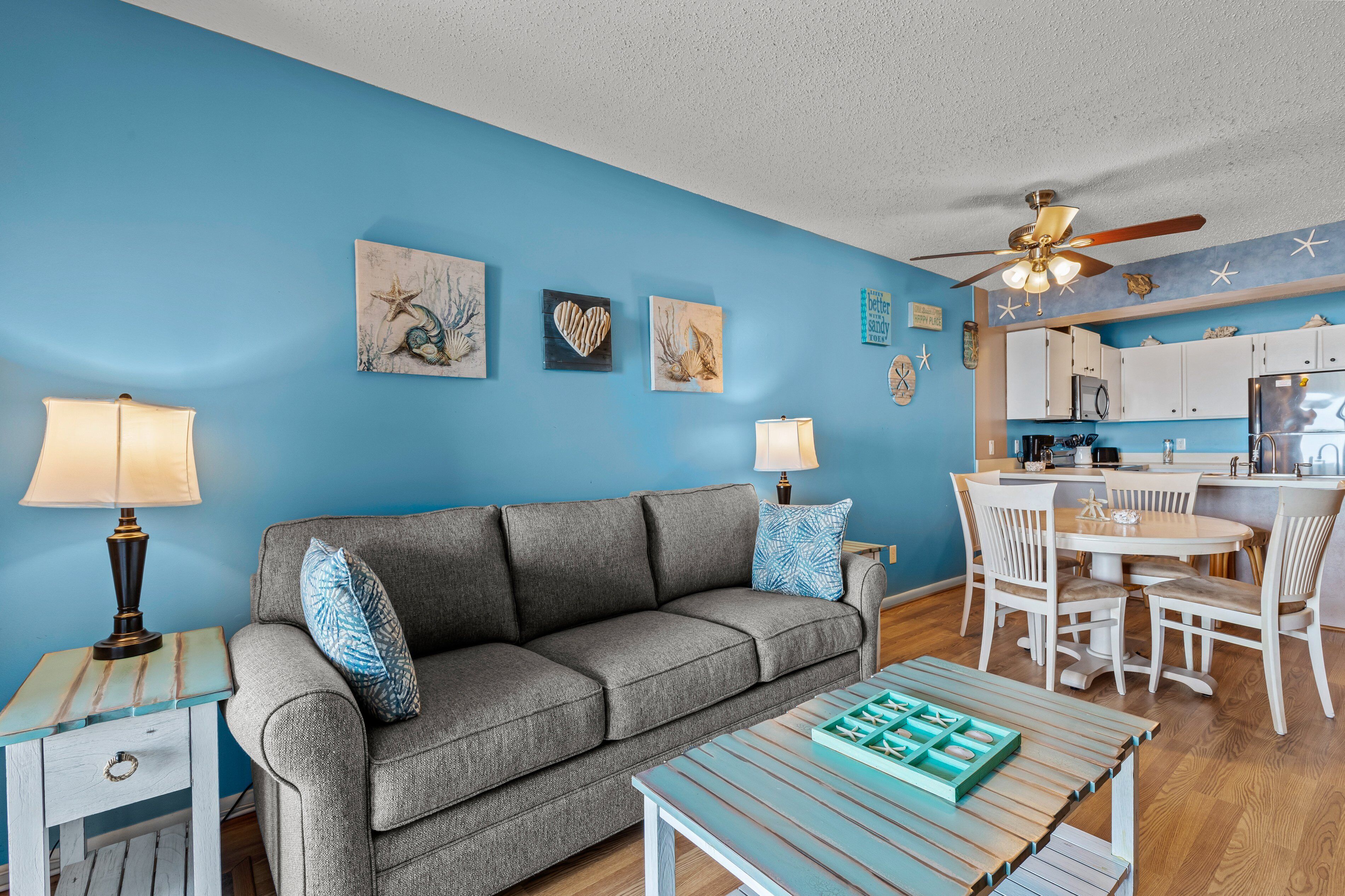 Ein Wohnzimmer mit grauem Sofa, blauen Wänden und Deckenventilator.