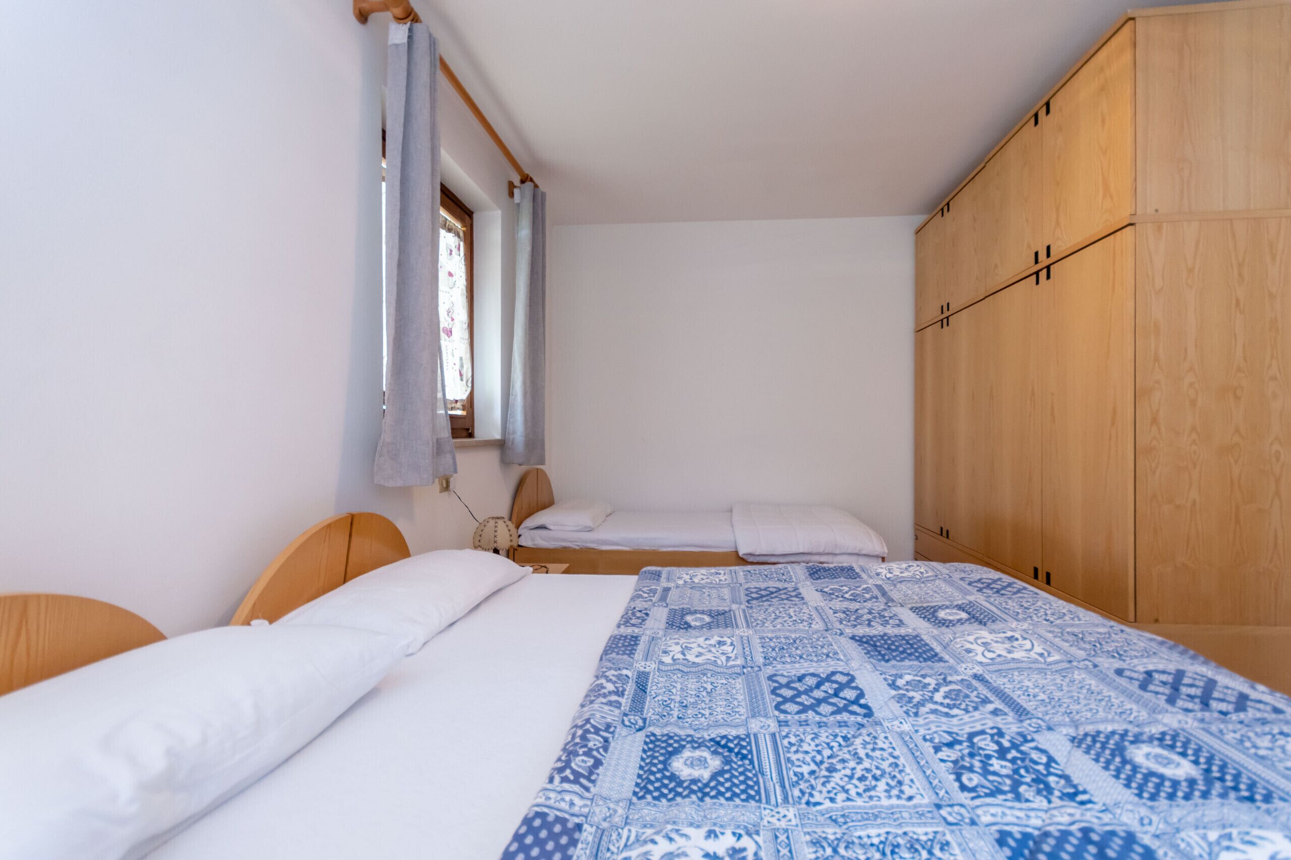 A bedroom with two beds, wooden headboards, a large wardrobe, and a patterned bedspread.