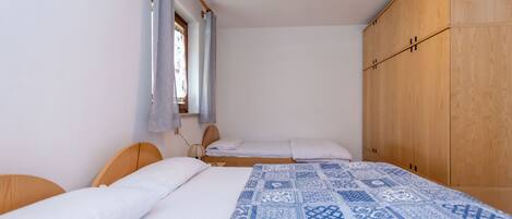 A bedroom with two beds, wooden headboards, a large wardrobe, and a patterned bedspread.
