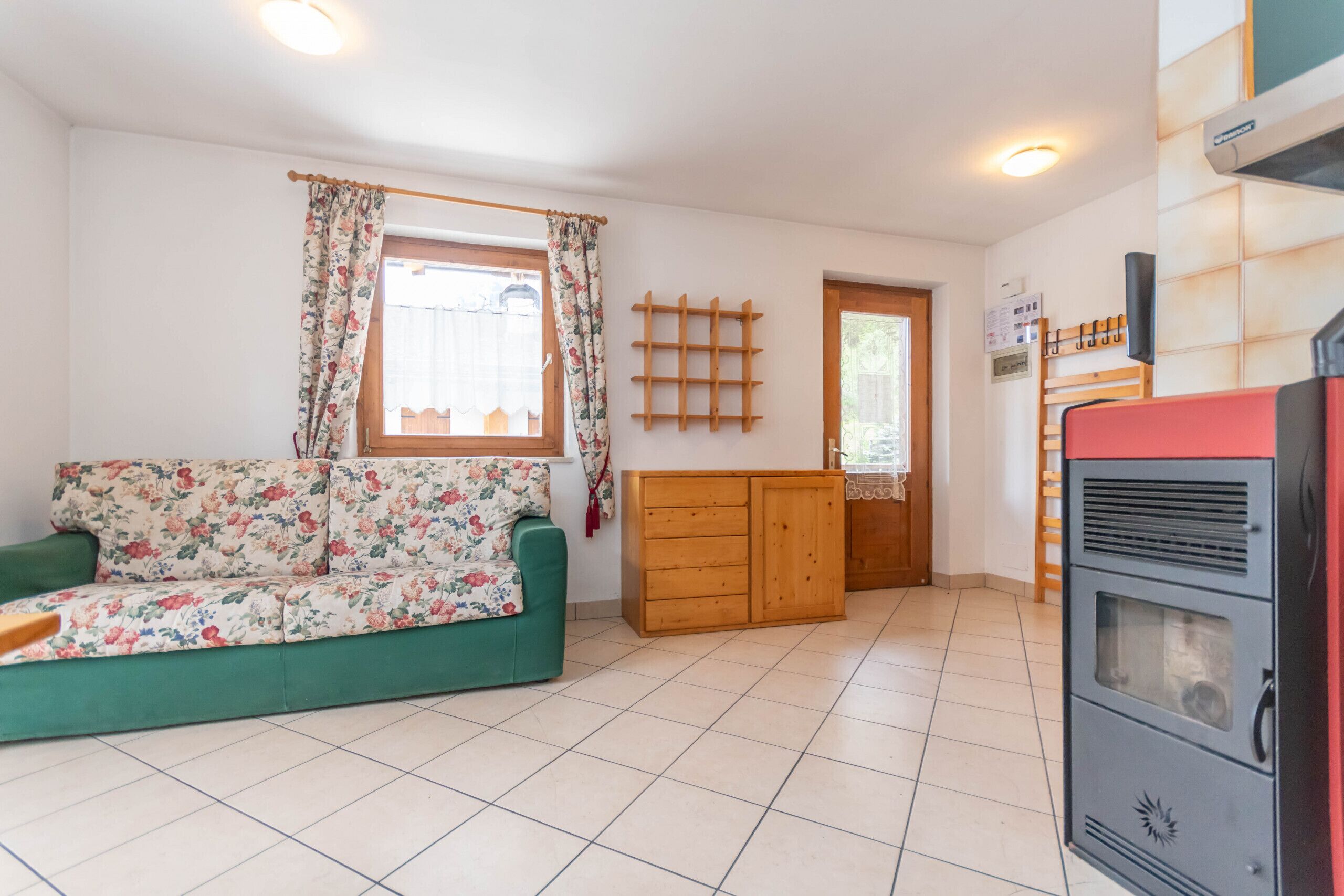 Un salon avec un canapé à motifs floraux, un meuble en bois, un appareil électroménager rouge et une fenêtre avec des rideaux.