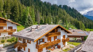 Un edificio de estilo chalet con techo inclinado, balcones de madera y vistas a una cadena montañosa boscosa.