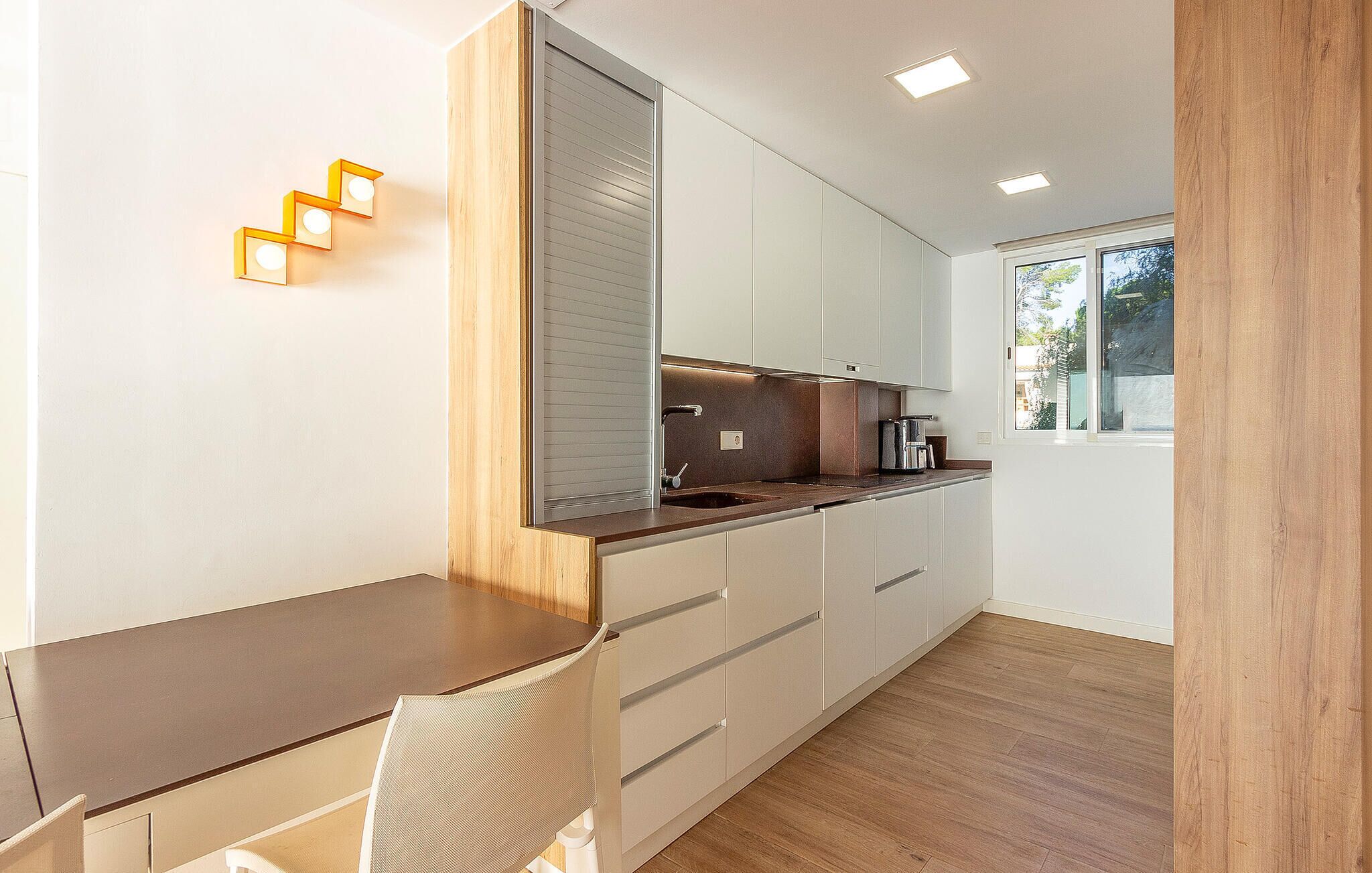 A modern kitchen with white cabinets, a wooden countertop, and a window providing natural light.