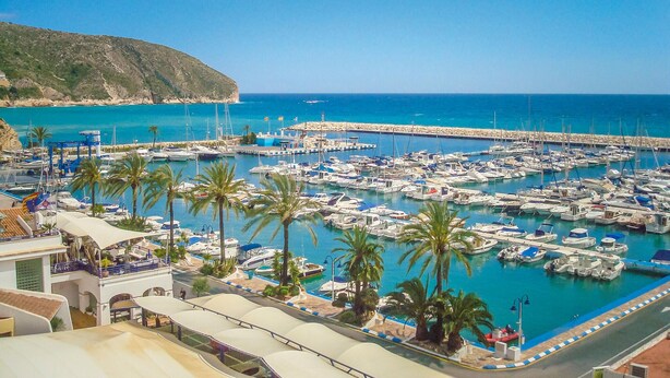 Un port de plaisance où sont amarrés de nombreux bateaux, une côte rocheuse et un ciel bleu dégagé.