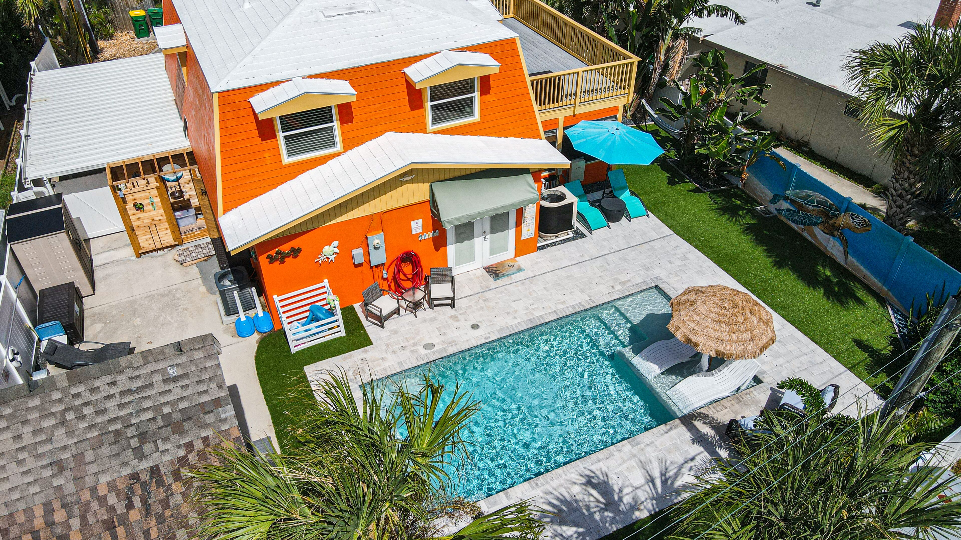 A two-story house with a swimming pool, outdoor furniture, and a thatched umbrella.