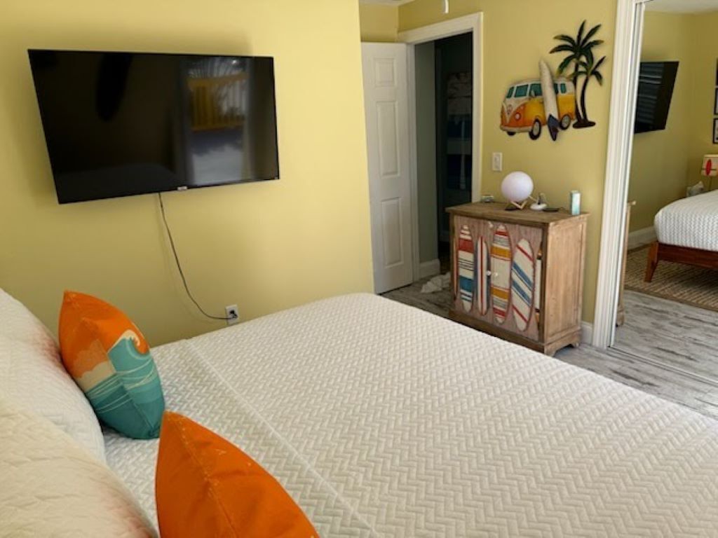 Een slaapkamer met een bed, een aan de muur bevestigde televisie, een houten dressoir en een deur naar een andere kamer.