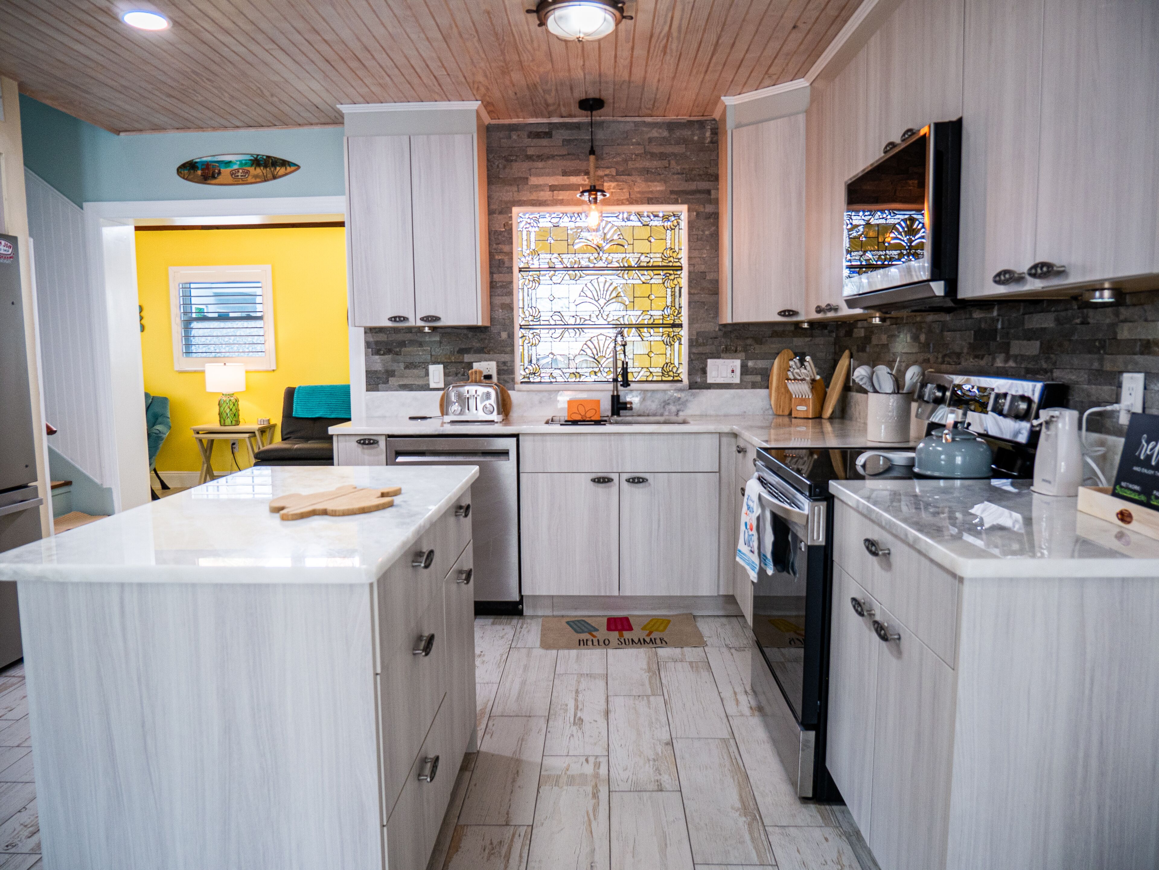 A modern kitchen with light wood cabinets, a central island, and a built-in oven.