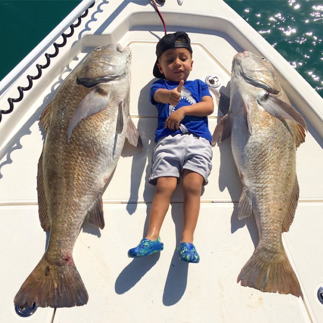 A child on a boat holding two large fish.