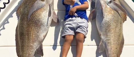 A child on a boat holding two large fish.