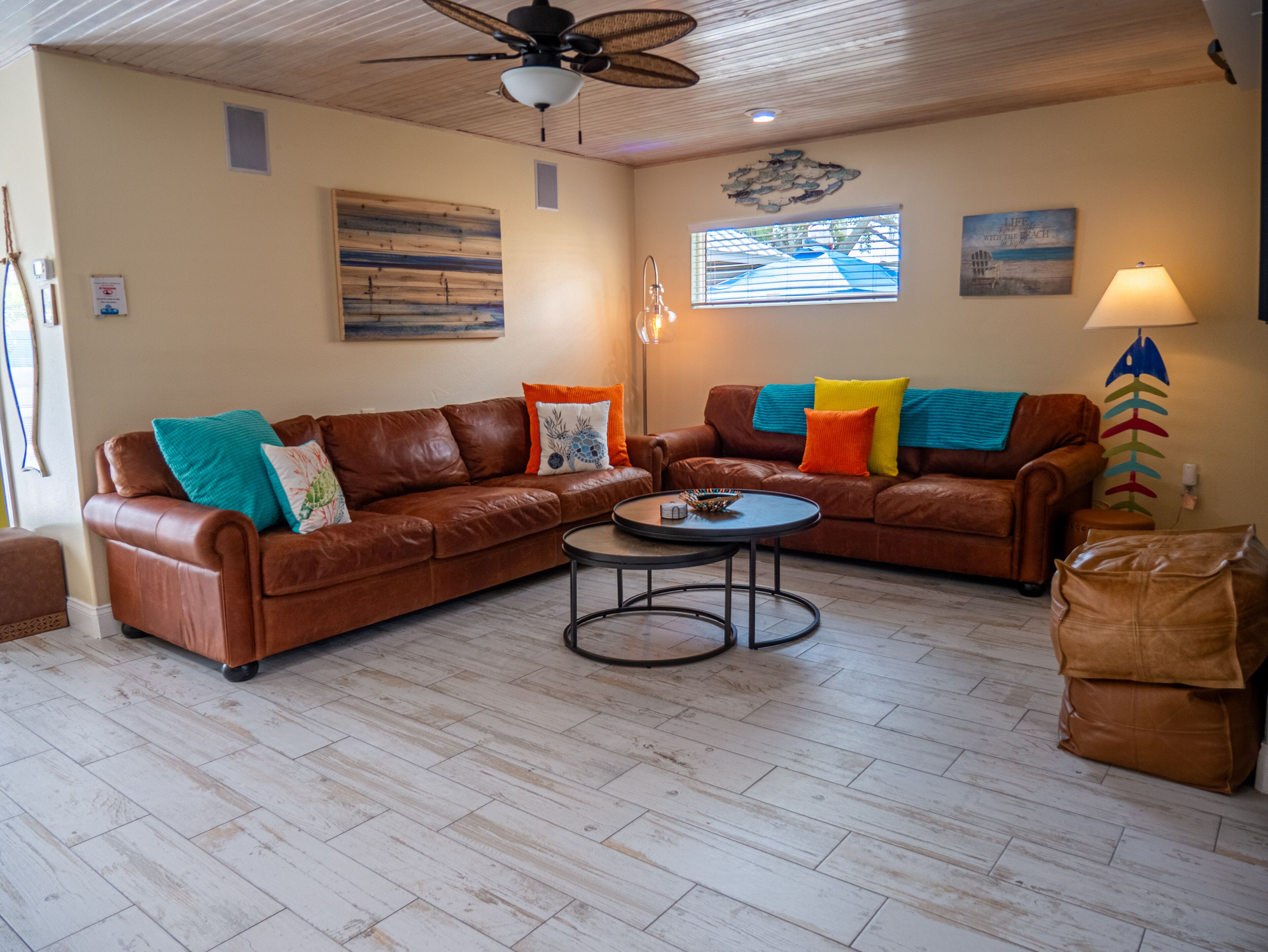 A spacious living room with two brown leather sofas, a round coffee table, and a ceiling fan.