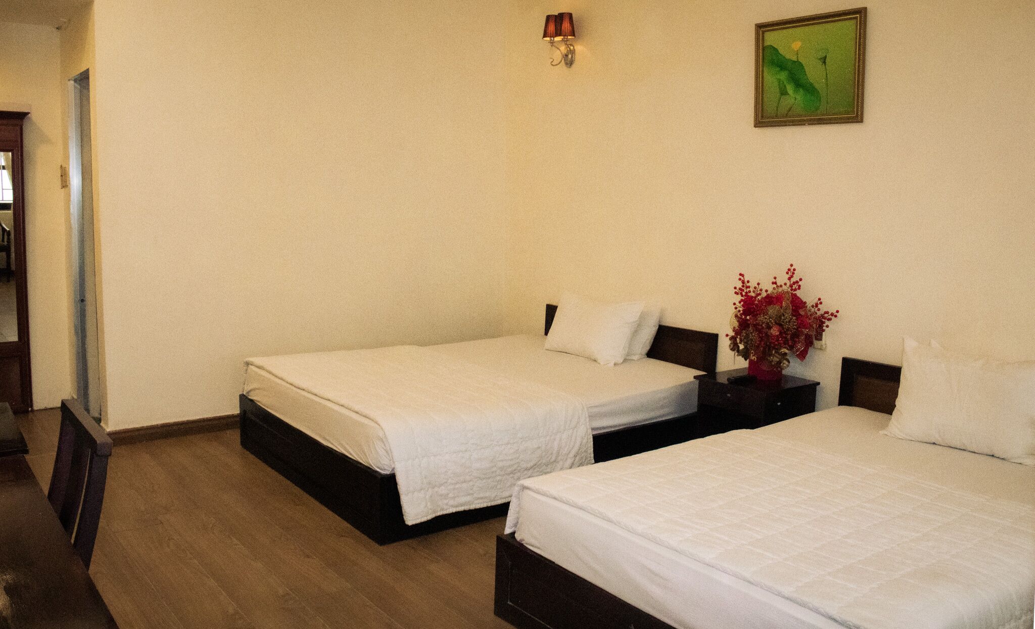 Habitación de hotel con dos camas individuales, una mesita de noche con un jarrón de flores, un cuadro en la pared y una lámpara.
