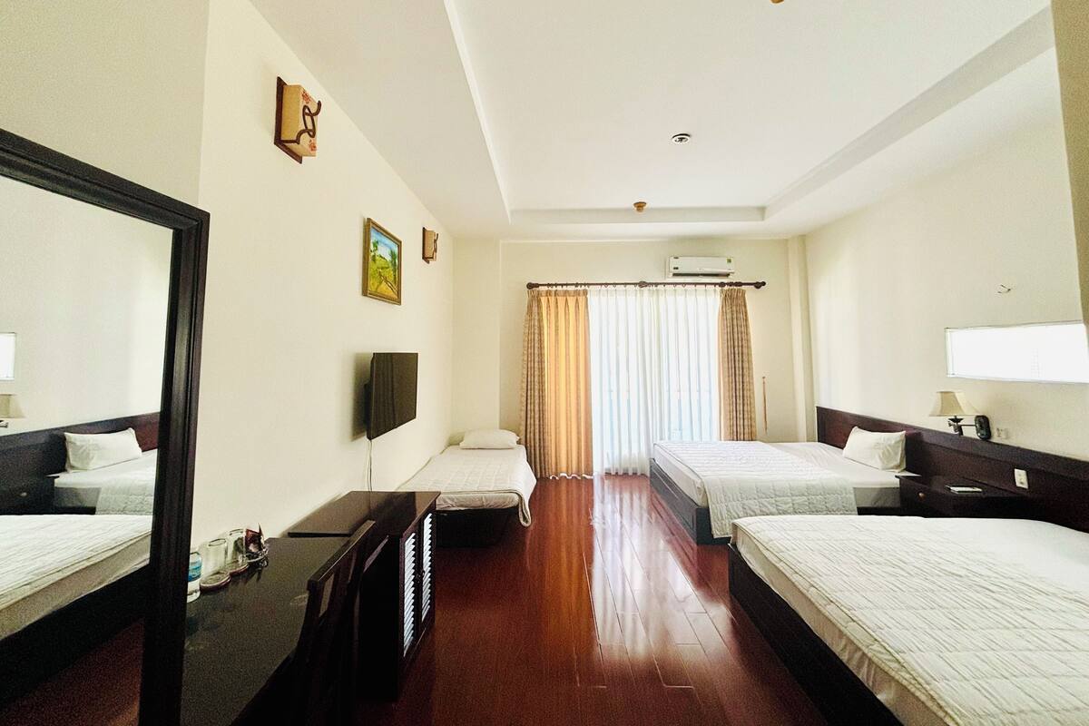 A hotel room with two beds, a TV, a desk, and a window with curtains.
