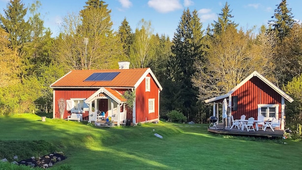 Two red wooden cabins with solar panels, surrounded by a lush green landscape and dense forest.