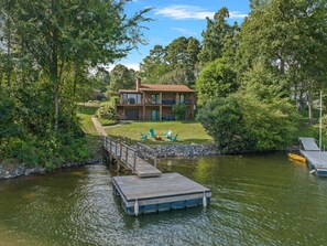 A lakeside cabin with a dock, a grassy deck, and a view of the surrounding forest.