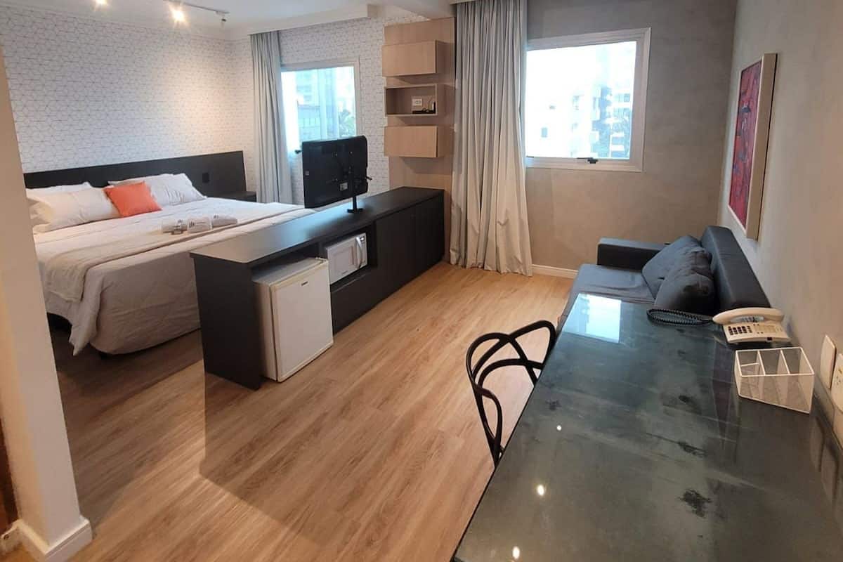 A modern hotel room with a bed, a desk, a sofa, and a dining table.