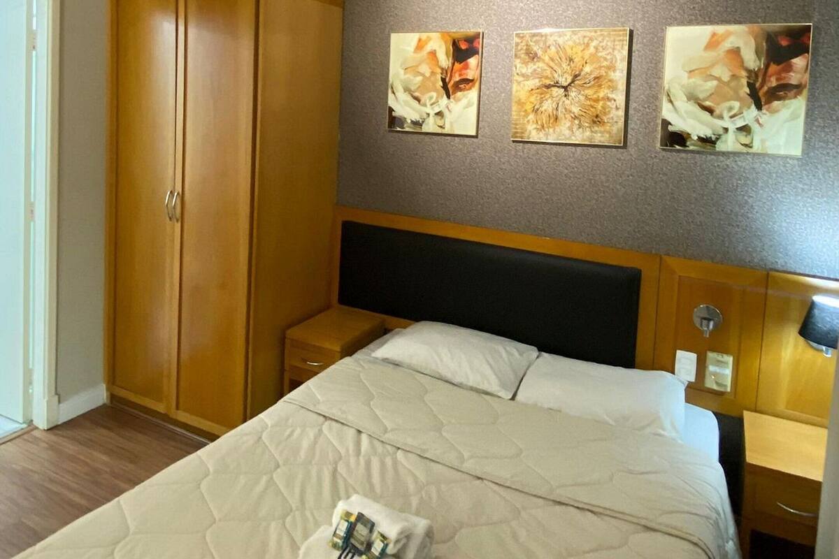 A hotel room with a bed, wooden wardrobe, and three paintings on the wall.
