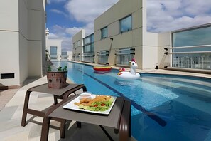 A rooftop pool with a dining table and chairs, a swan float, and a small building with plants. - Studio Living Oscar Freire (São Paulo)
