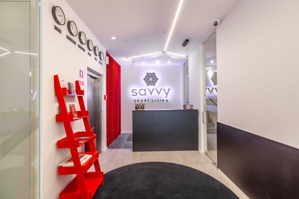 Una zona de recepción con diseño moderno, que incluye un mostrador negro, un logotipo en la pared y una estantería roja.