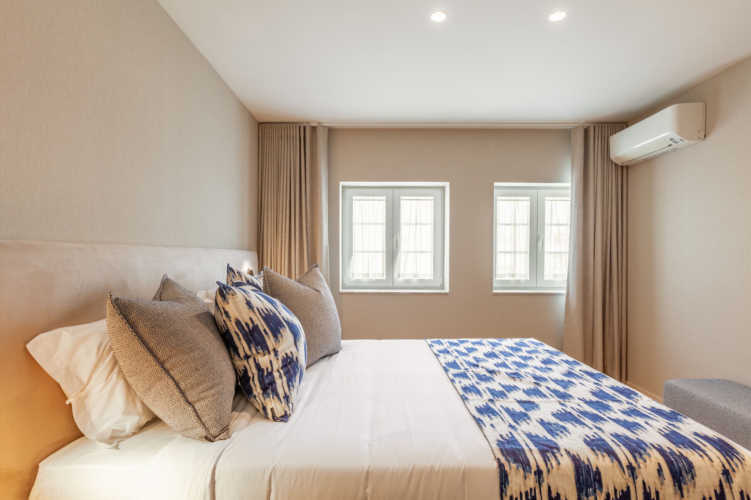 Ein Hotelzimmer mit einem großen Bett, beigen Wänden und zwei mit Vorhängen versehenen Fenstern.