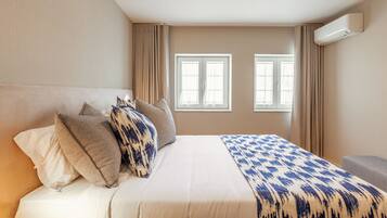 Ein Hotelzimmer mit einem großen Bett, beigen Wänden und zwei mit Vorhängen versehenen Fenstern.