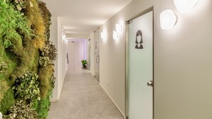 A hallway with a vertical garden, a lighted wall, and a door with a person silhouette. - ing (Oporto)