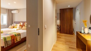 A hotel room with two beds, a wooden floor, a desk with a vase, and a sliding door leading to another room. - ing (Oporto)