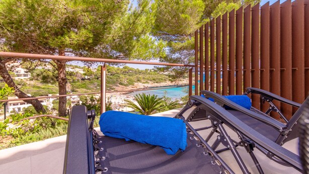 A balcony with a view of a beach and turquoise waters. There are two lounge chairs with blue cushions. - Cala Mendia Beach House 2 es with direct access to the beach and sea views (Portocristo - Cala Mandia)