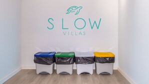 A wall with the text "SLOW VILLAS" and four trash bins in blue, green, white, and yellow. - Cala Mendia Beach House 2 es with direct access to the beach and sea views (Portocristo - Cala Mandia)