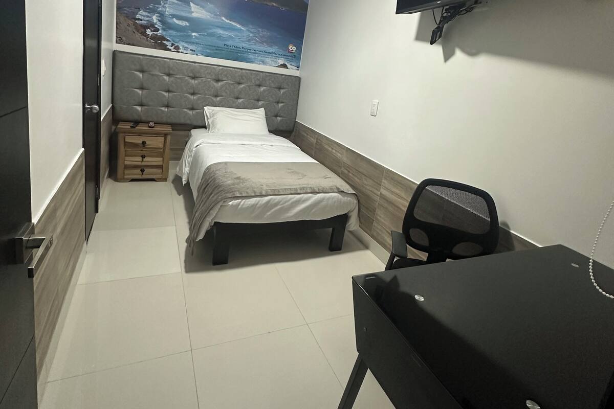 Une chambre à coucher avec un lit, un bureau, une chaise, un téléviseur et une affiche accrochée au mur.