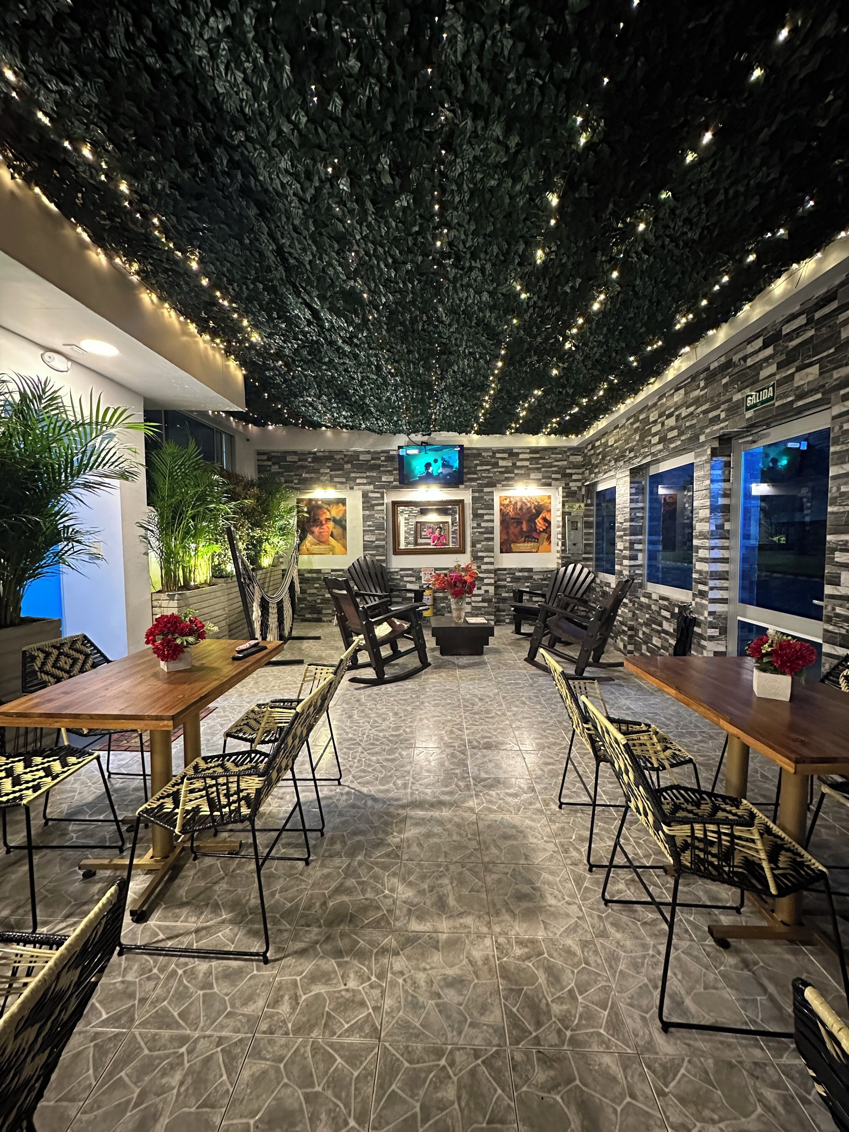 A restaurant with a stone-tiled floor, wooden tables and chairs, and a ceiling with hanging lights.