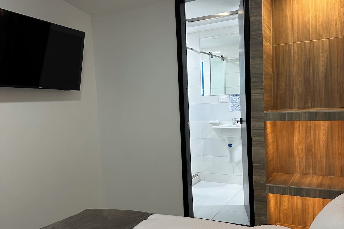 Une chambre d’hôtel moderne, dotée d’un lit, d’un téléviseur à écran plat fixé au mur et d’un panneau décoratif en bois sur le mur.