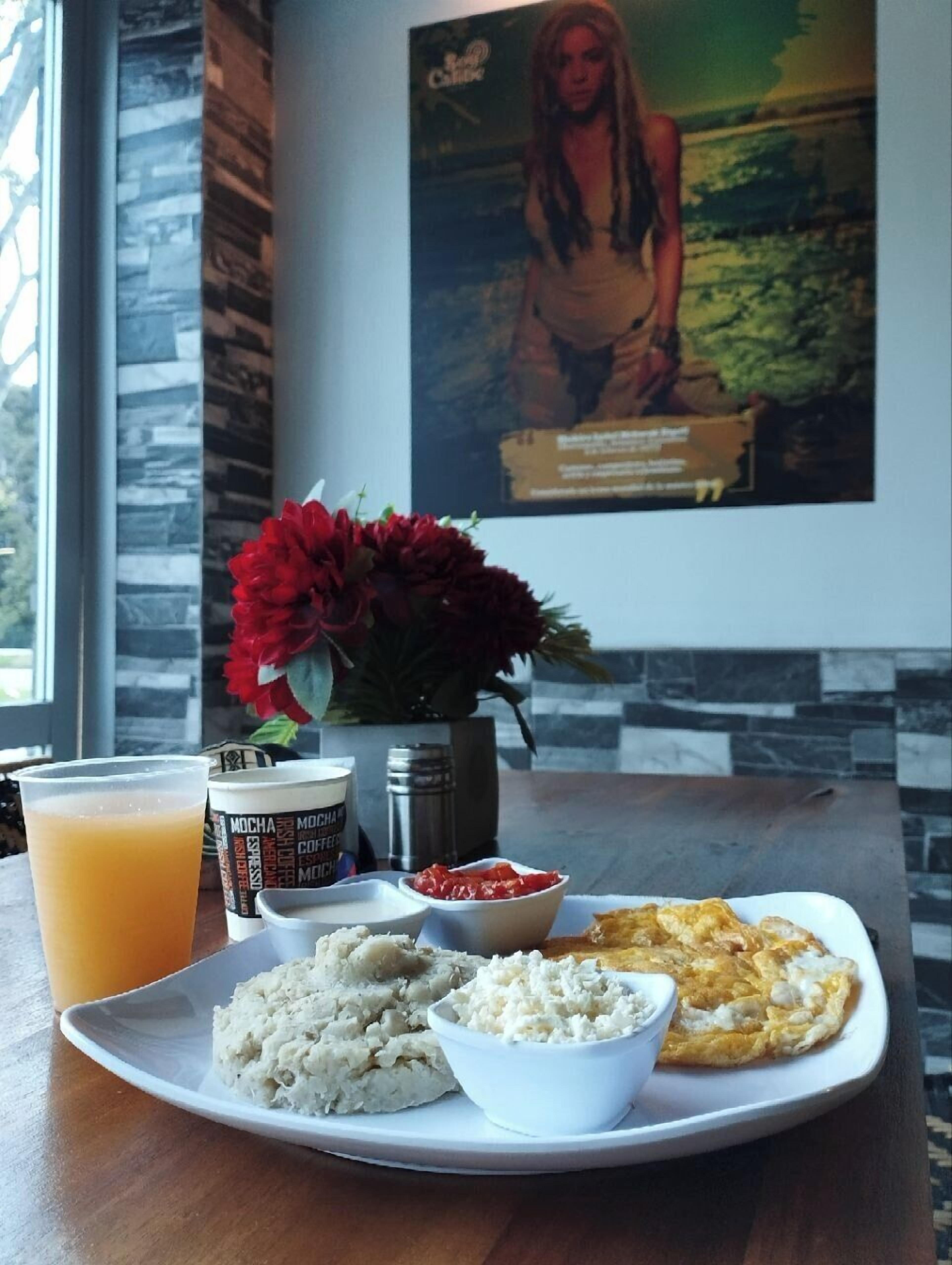 A breakfast plate with rice, a bowl of sauce, and a fried egg on a table with a drink and a coffee cup.