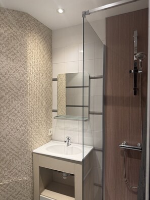 Une salle de bain moderne avec une douche à parois de verre, un lavabo blanc et un meuble-lavabo en bois.