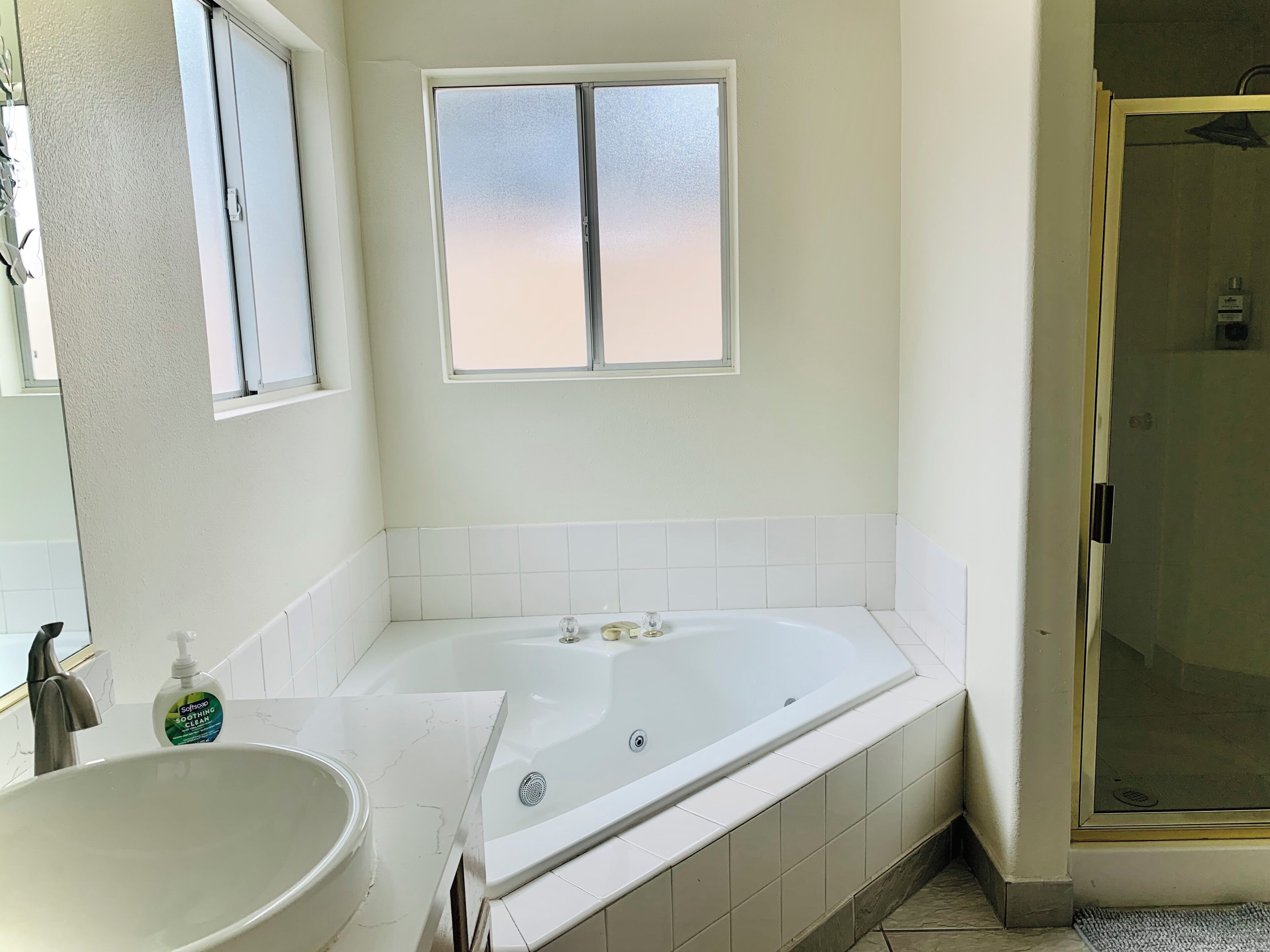 A bathroom with a large bathtub, a sink, a window, and a shower area.