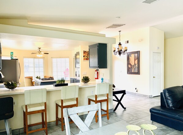 A modern kitchen with a central island, bar stools, and a dining area with a black leather couch. - 4 bedrooms house. Sleeps 14, 13 miles to Airport, 7-11 miles to the Strip. (North Las Vegas)