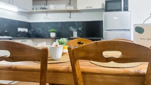 Eine moderne Küche mit weißen Schränken, einer Mikrowelle und einem Kühlschrank. Holzstühle mit gewebten Tischsets und ein kleiner Topf stehen auf der Arbeitsplatte.