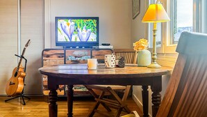 Ein Wohnzimmer mit einem Holzesstisch, einer Gitarre, einem Fernseher und einer Lampe.