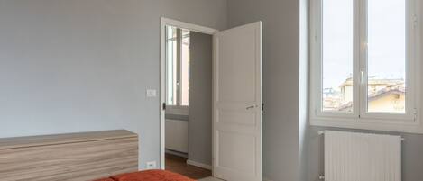 A bedroom with a bed, a window, and a door leading to a hallway.
