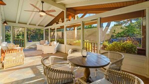 Un patio couvert aménagé avec des meubles en osier, une table ronde et un ventilateur de plafond.
