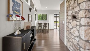 Un intérieur moderne avec un mur en pierre, un coin repas en bois et une console noire agrémentée d’objets décoratifs.