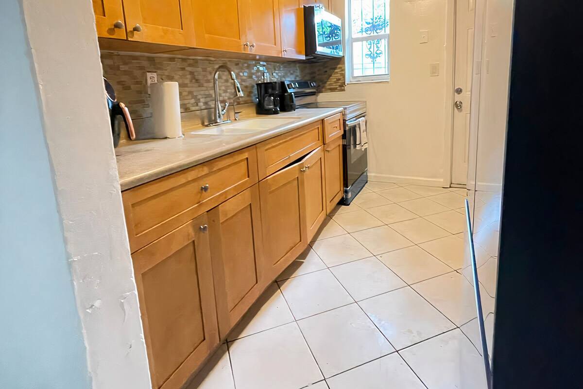 Una cocina con armarios de madera, un lavamanos de acero inoxidable y un refrigerador negro.