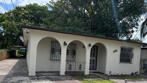 A single-story house with a white exterior, three arched windows, and a black metal gate.