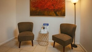A room with two chairs, a painting of a tree, and a lamp.