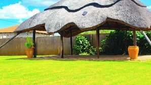 A thatched-roof structure with a solar panel, surrounded by a well-maintained lawn and potted plants. - Bulawayo Bliss - Cozy 3 Bedroom House (Bulawayo)