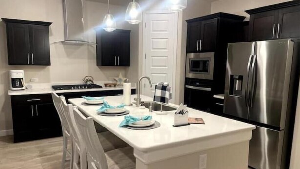 A modern kitchen with dark cabinets, stainless steel appliances, and a white island with bar stools. - Las Cruces, New 4BR home, Vacation, Games, Pickleball, Family Friendly (Las Cruces)