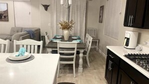 A compact kitchen with a dining area, a coffee maker, and a wall-mounted light fixture. - Las Cruces, New 4BR home, Vacation, Games, Pickleball, Family Friendly (Las Cruces)
