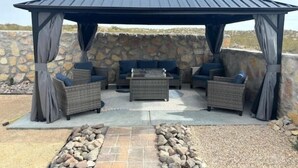 A covered outdoor seating area with wicker furniture and a stone wall backdrop. - Las Cruces, New 4BR home, Vacation, Games, Pickleball, Family Friendly (Las Cruces)