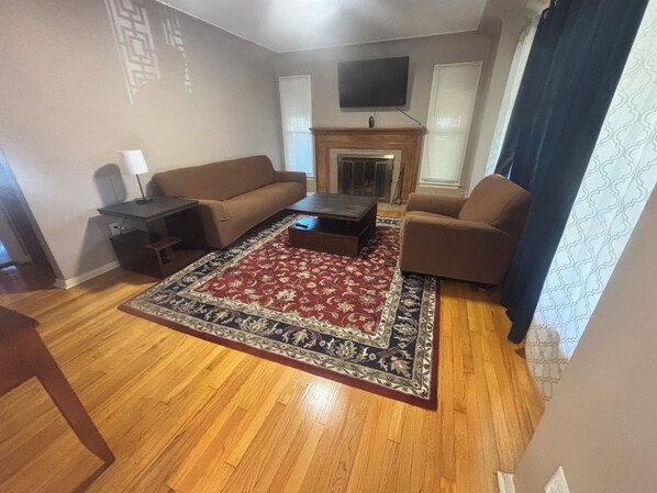 Una sala de estar con sofá, una mesa de centro, un televisor montado en la pared y una chimenea.