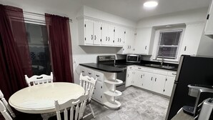 Uma cozinha compacta com armários brancos, micro-ondas, pia e um espaço de refeições com mesa e cadeiras.