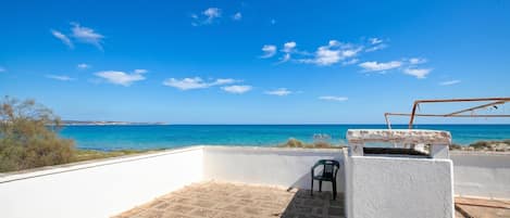 A rooftop terrace with a view of the sea, a white wall, and a green chair.